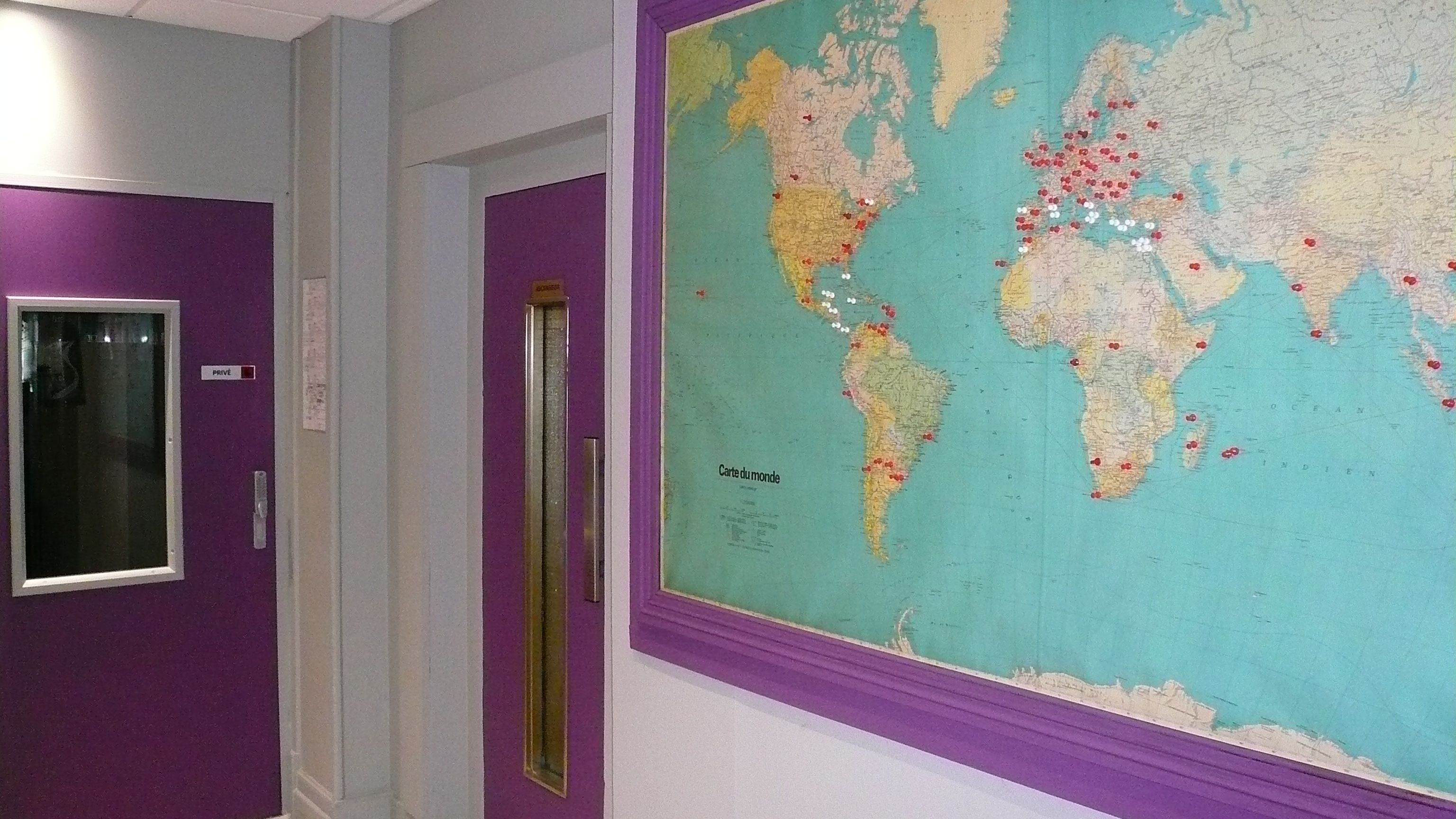 A hallway with a purple door, a window, and a large world map on the wall.