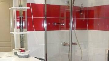 A modern bathroom with a glass shower enclosure, a white sink with a mirror, and red-tiled walls.