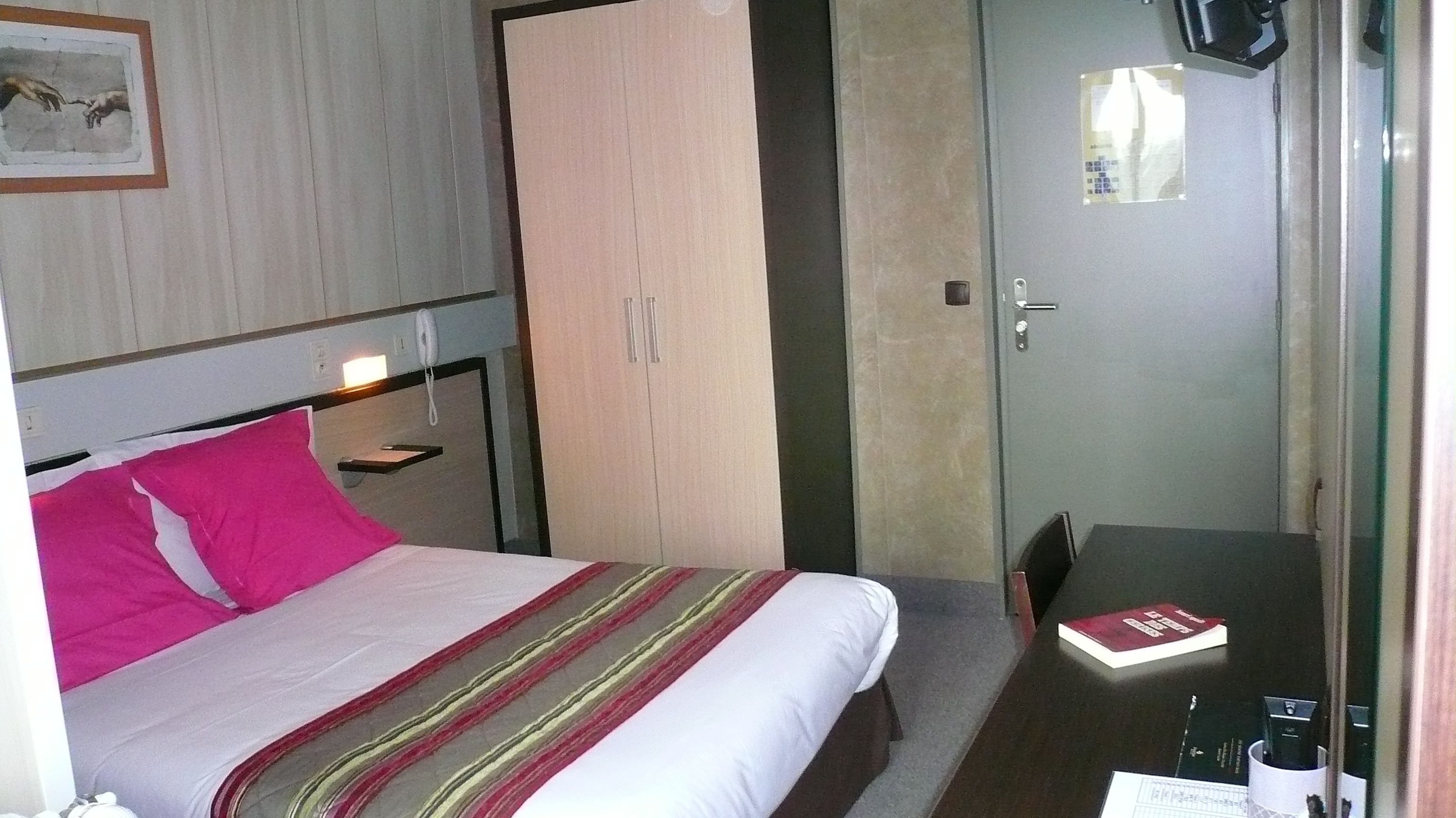 Une chambre d’hôtel comprenant un lit, une table de chevet, une armoire, un bureau avec une chaise et une porte.