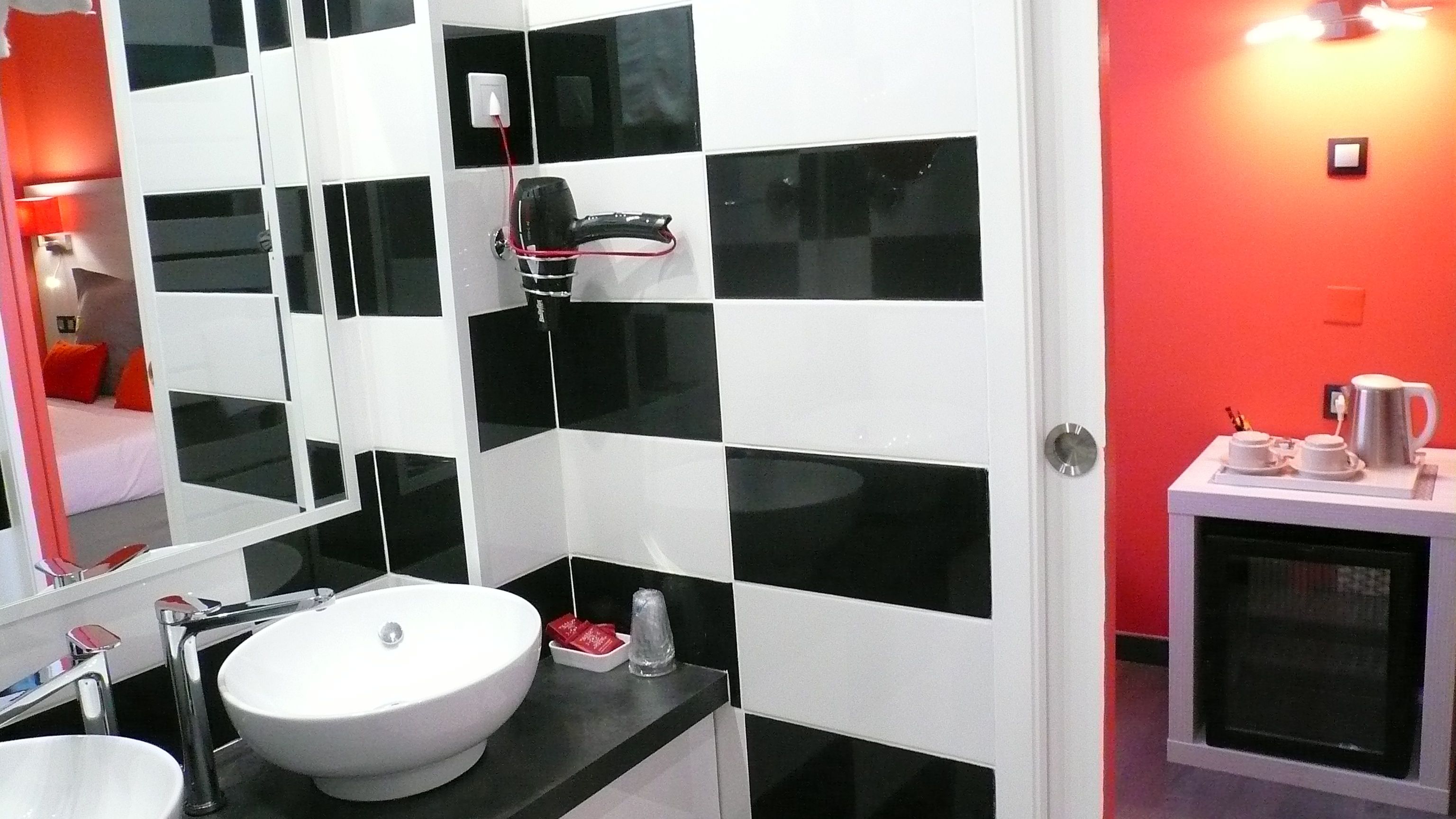 A modern bathroom with a white sink, black and white tiles, a hairdryer, and a coffee machine.