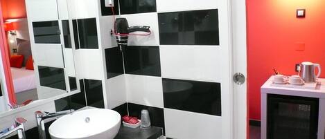 A modern bathroom with a white sink, black and white tiles, a hairdryer, and a coffee machine.