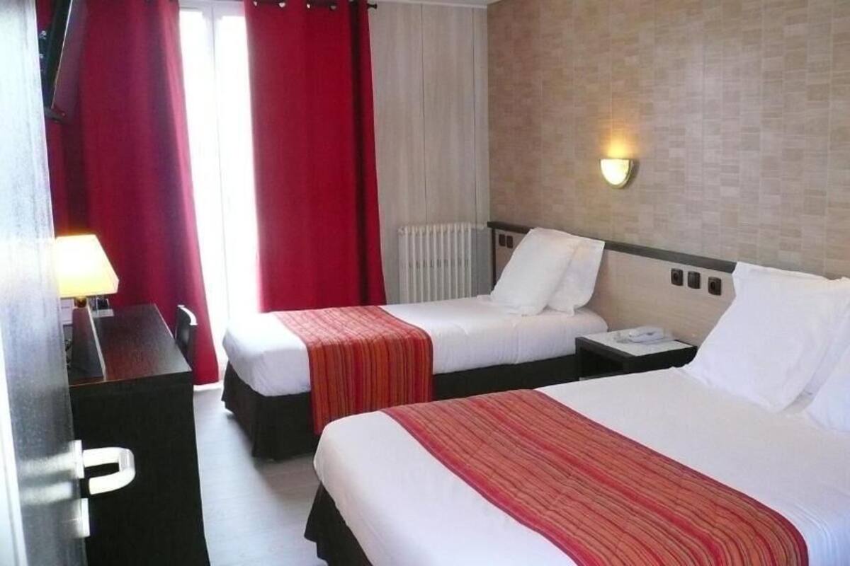 A hotel room with two beds, a desk, and a lamp.