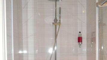 A glass-enclosed shower with a handheld showerhead and a wall-mounted faucet.