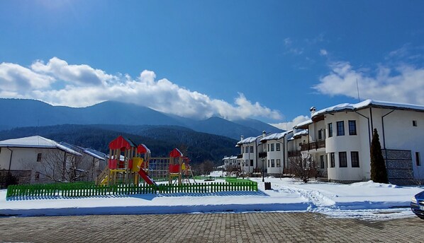 A snowy residential area with a playground, houses, and mountains in the background. - Pinerose Resort (Bansko)