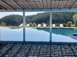 A pool with clear blue water, surrounded by lounge chairs and a view of a forested hillside. - Pinerose Resort (Bansko)