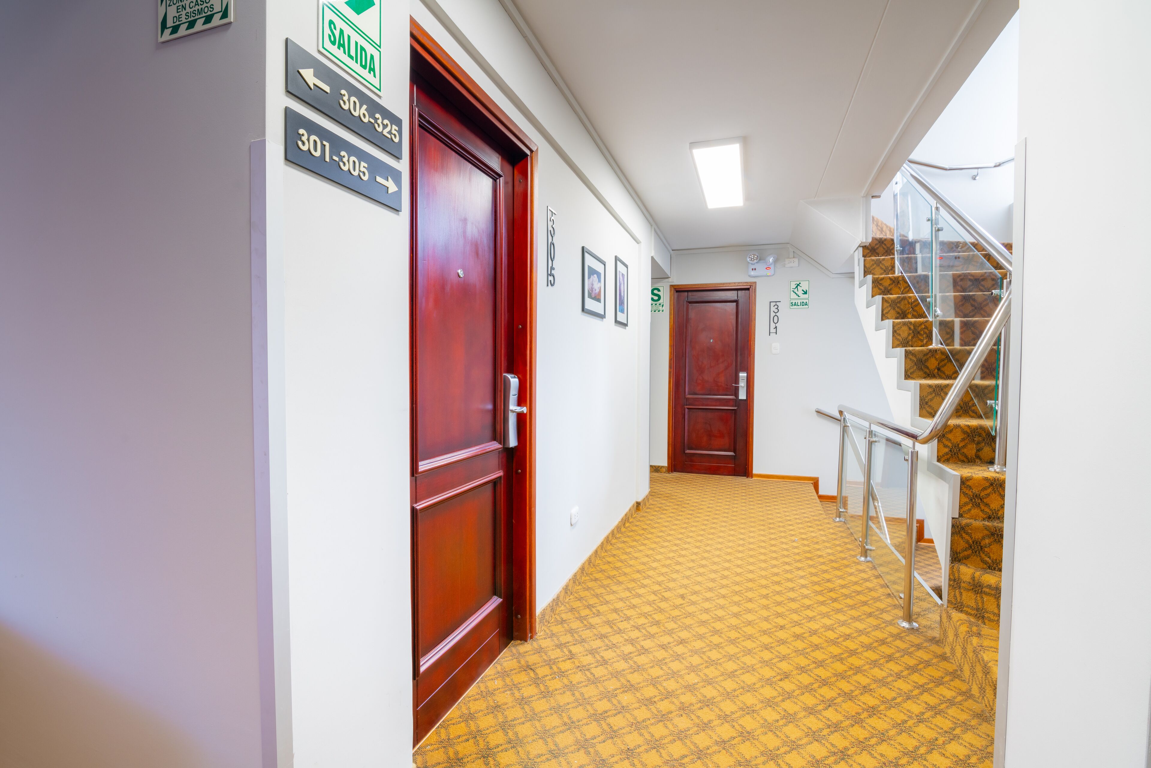 A hallway with wooden doors, a yellow patterned carpet, and a staircase with glass railings.