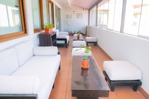 Um hall de hotel com um sofá comprido, uma mesa de centro e várias plantas em vasos.