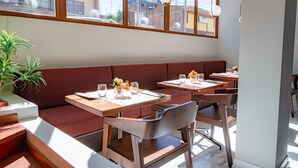 A restaurant with wooden tables and benches, large windows, and a potted plant. - El Tumi (Huaraz)