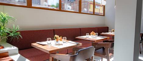 A restaurant with wooden tables and benches, large windows, and a potted plant.