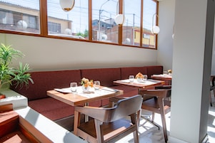 Un restaurante con mesas y bancos de madera, ventanas amplias y una planta en maceta.
