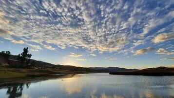 Un lago sereno que refleja el cielo con nubes dispersas, rodeado de colinas cubiertas de hierba y algunos árboles.