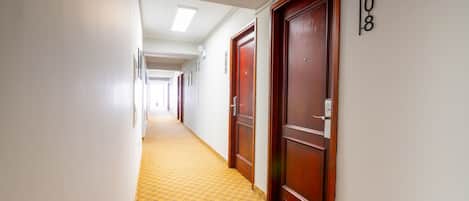 A hotel hallway with wooden doors, a yellow patterned carpet, and a number sign on the wall.