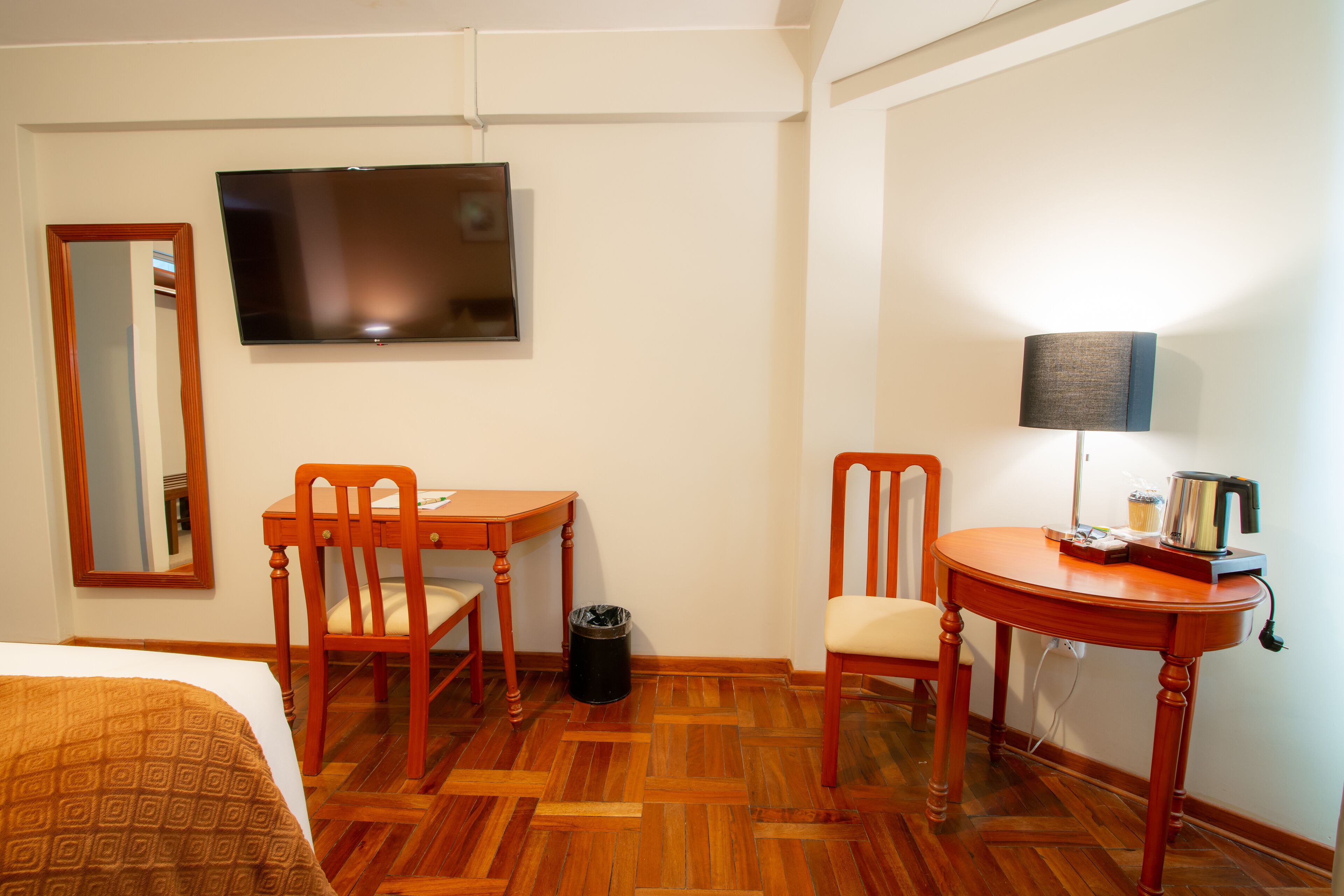 A hotel room with a bed, a wooden desk, two chairs, a television, a lamp, and a trash can.