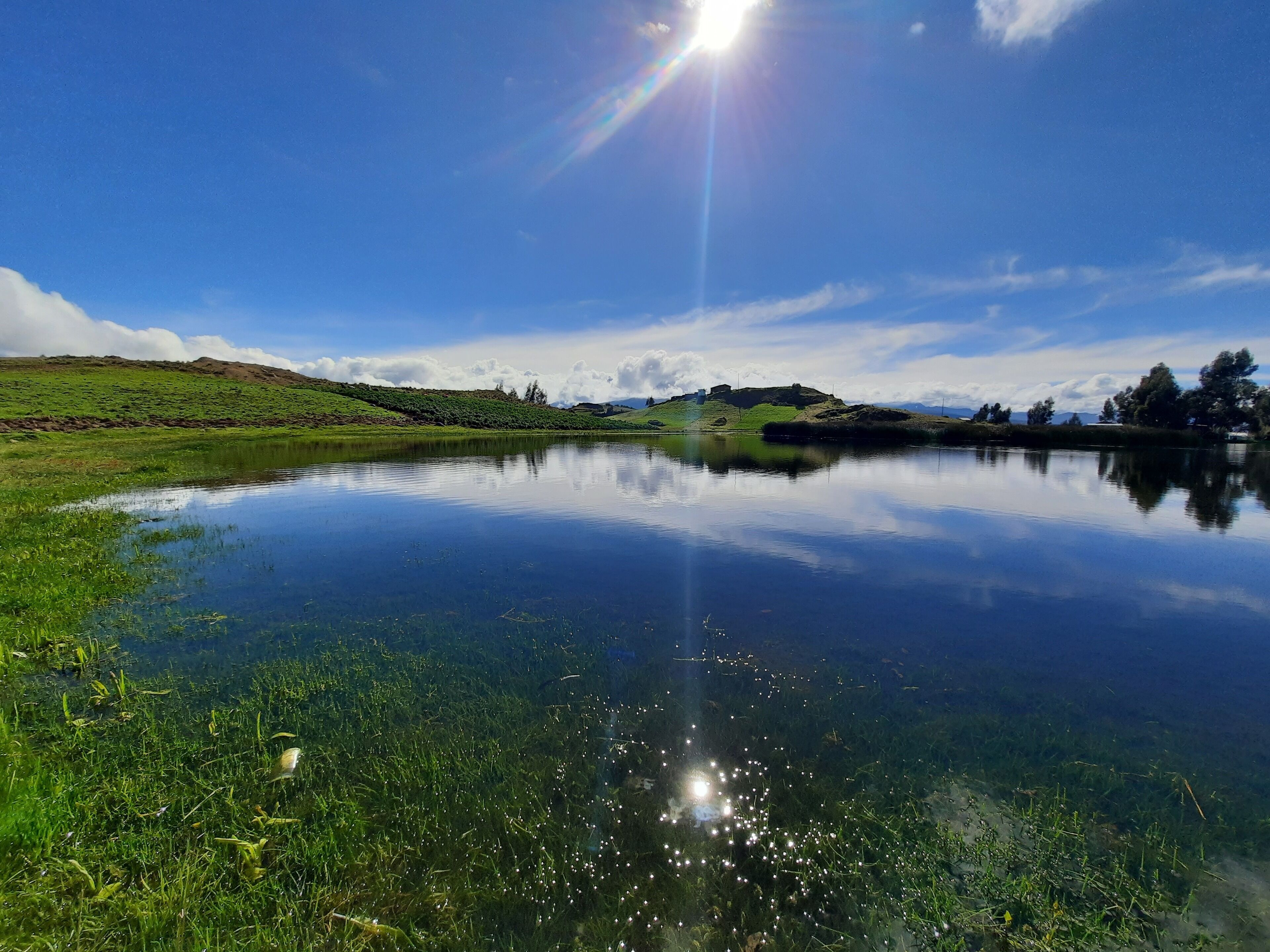 A calm lake with clear reflections, surrounded by green hills and a clear sky.