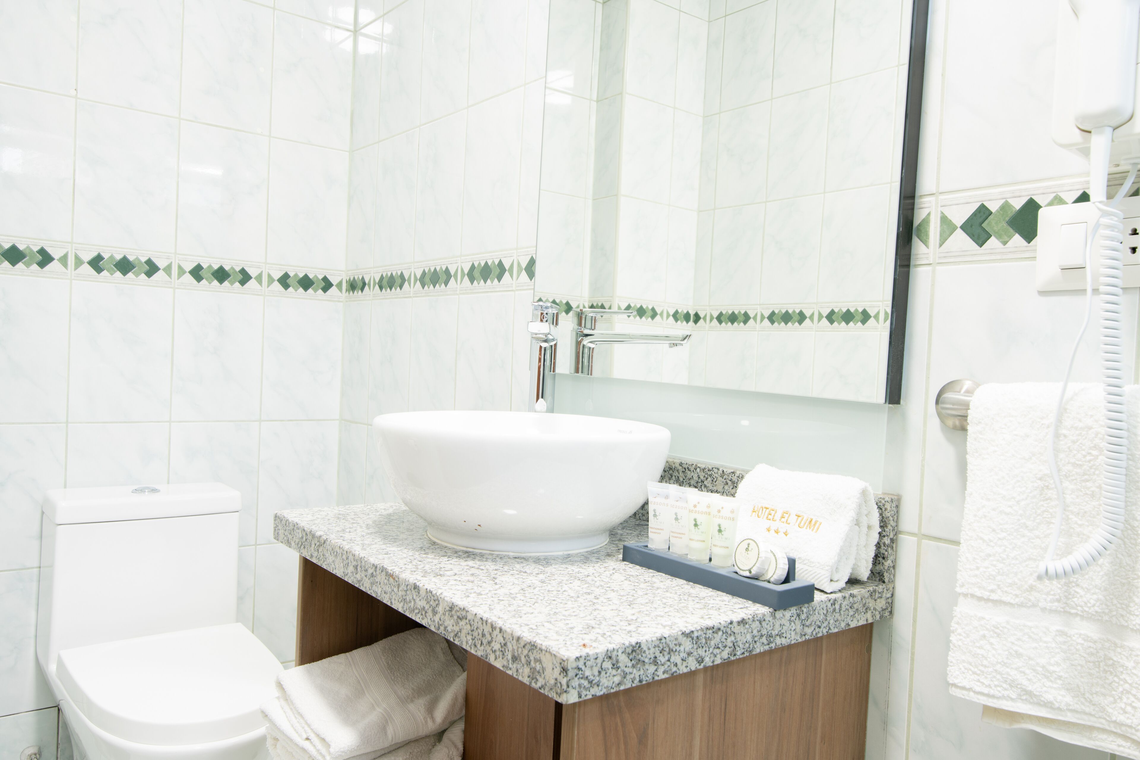 A bathroom with a white sink, a toilet, and a mirror. There are towels and toiletries on the counter.