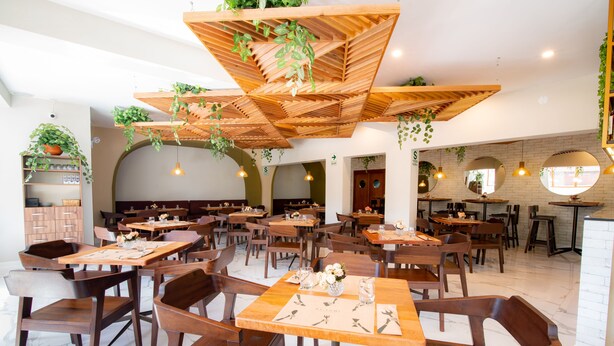 A spacious restaurant with wooden tables and chairs, hanging plants, and pendant lighting. - El Tumi (Huaraz)