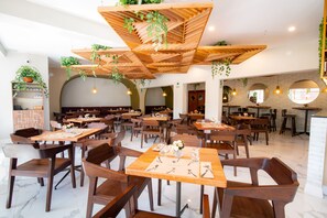 Un restaurante espacioso con mesas y sillas de madera, plantas colgantes e iluminación colgante.