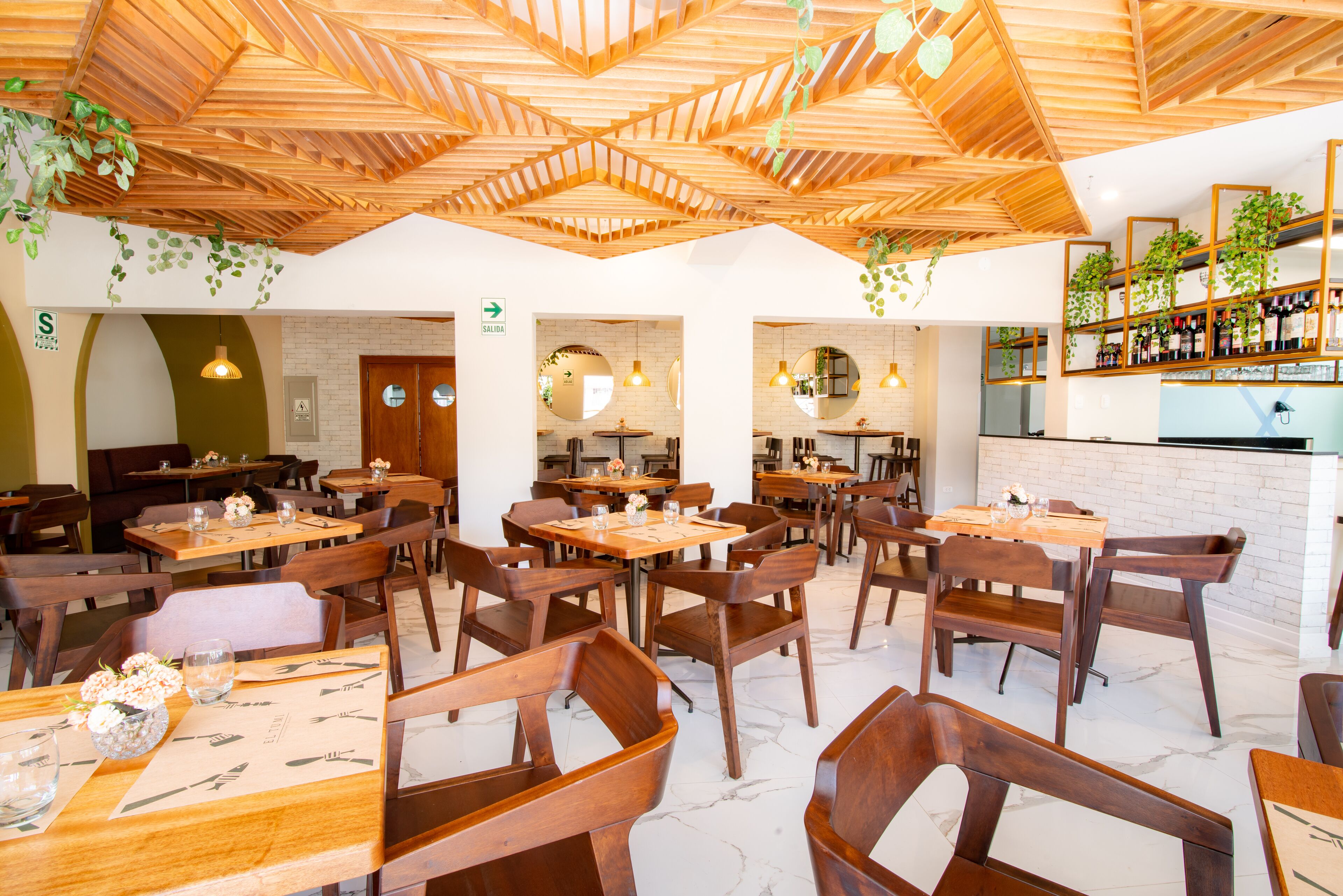 A restaurant interior with wooden tables and chairs, a brick wall, and hanging plants.
