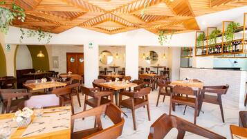 A restaurant interior with wooden tables and chairs, a brick wall, and hanging plants.