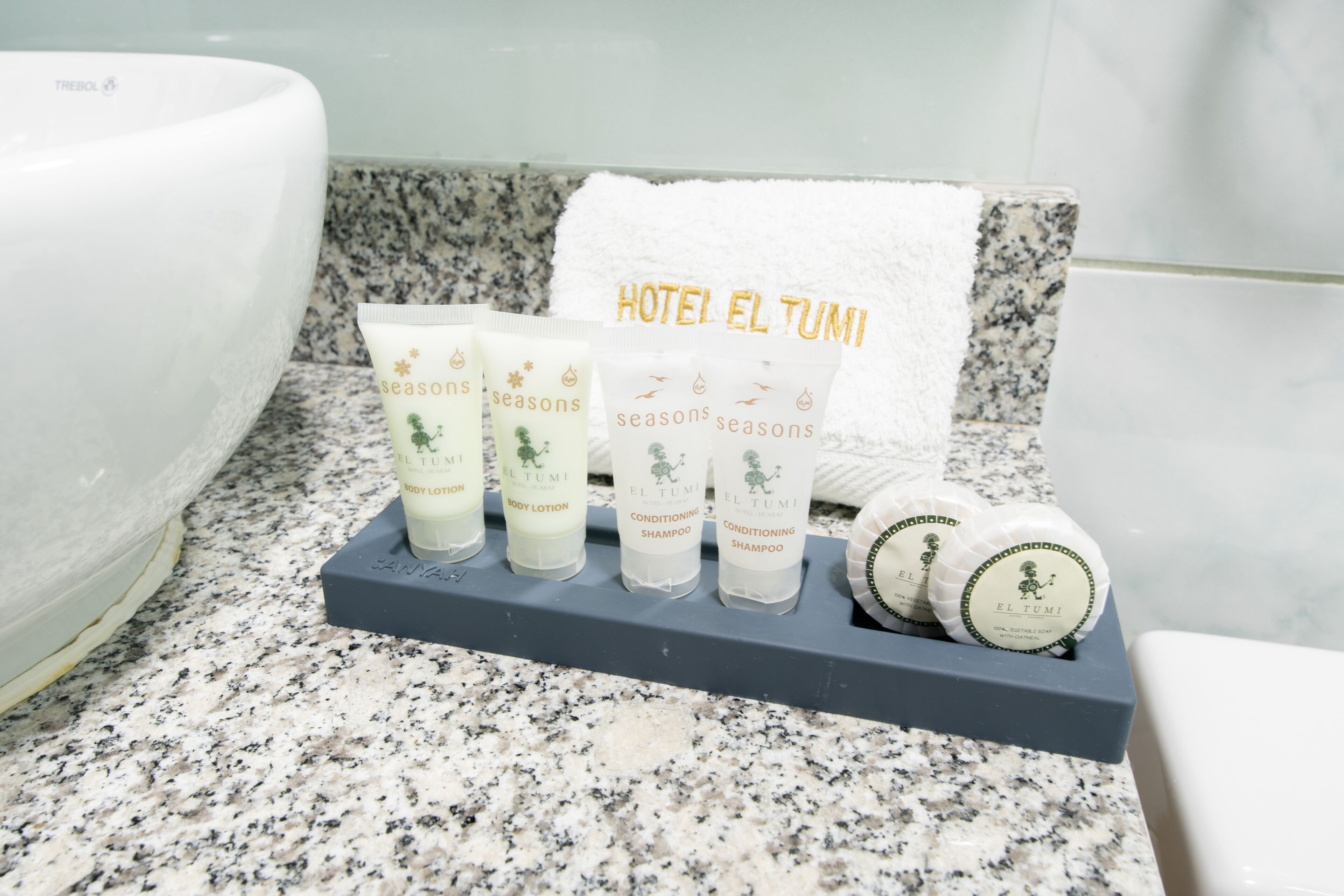 A bathroom with a granite countertop, a white bathtub, and a towel rack holding toiletries labeled 'Hotel El Tumi'.