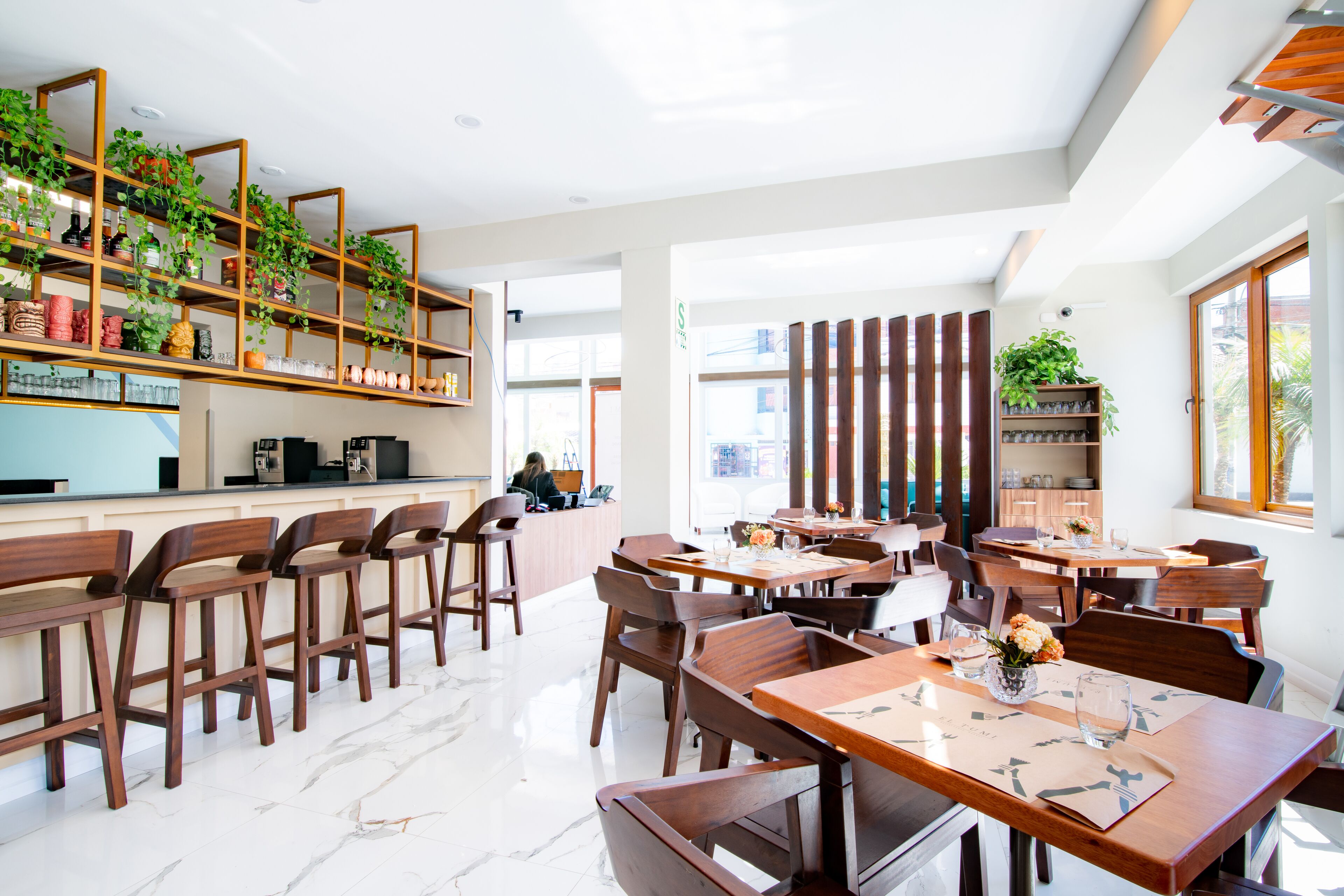 A modern restaurant with wooden furniture, a bar area, and shelves with plants.