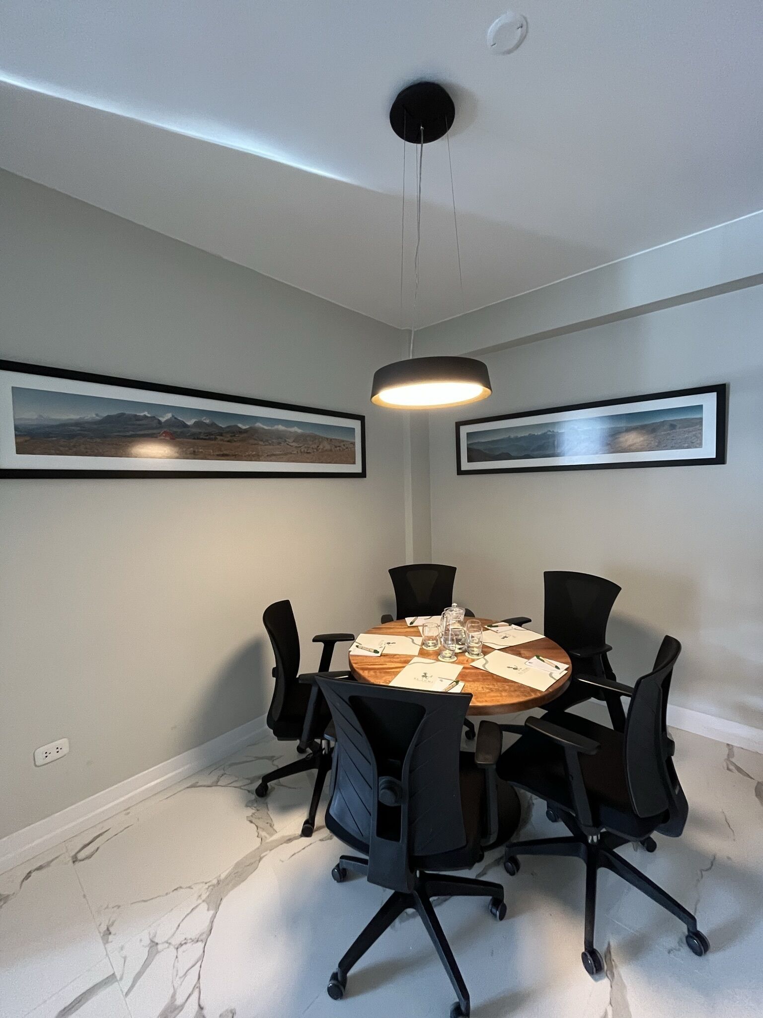 Une salle de conférence avec une table ronde, des chaises de bureau noires, des tableaux encadrés accrochés aux murs et un luminaire au plafond.