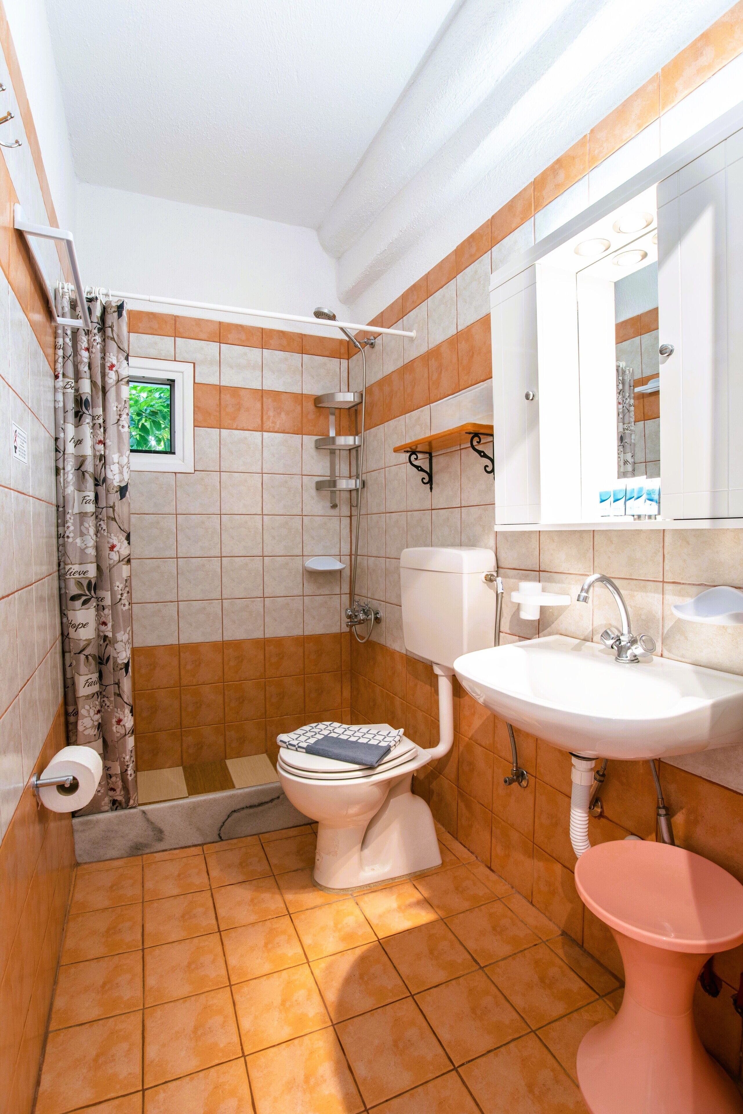 A bathroom with a toilet, sink, shower, and a small window.