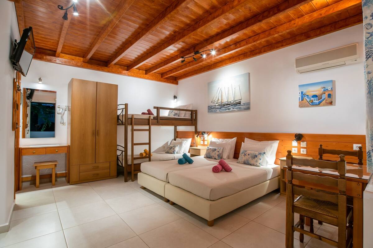 A bedroom with a bunk bed, wooden ceiling, and a desk with a chair.