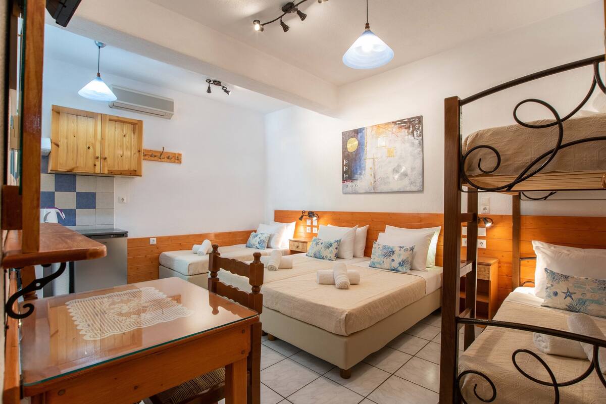 A compact room with two beds, a wooden table, and a kitchenette.