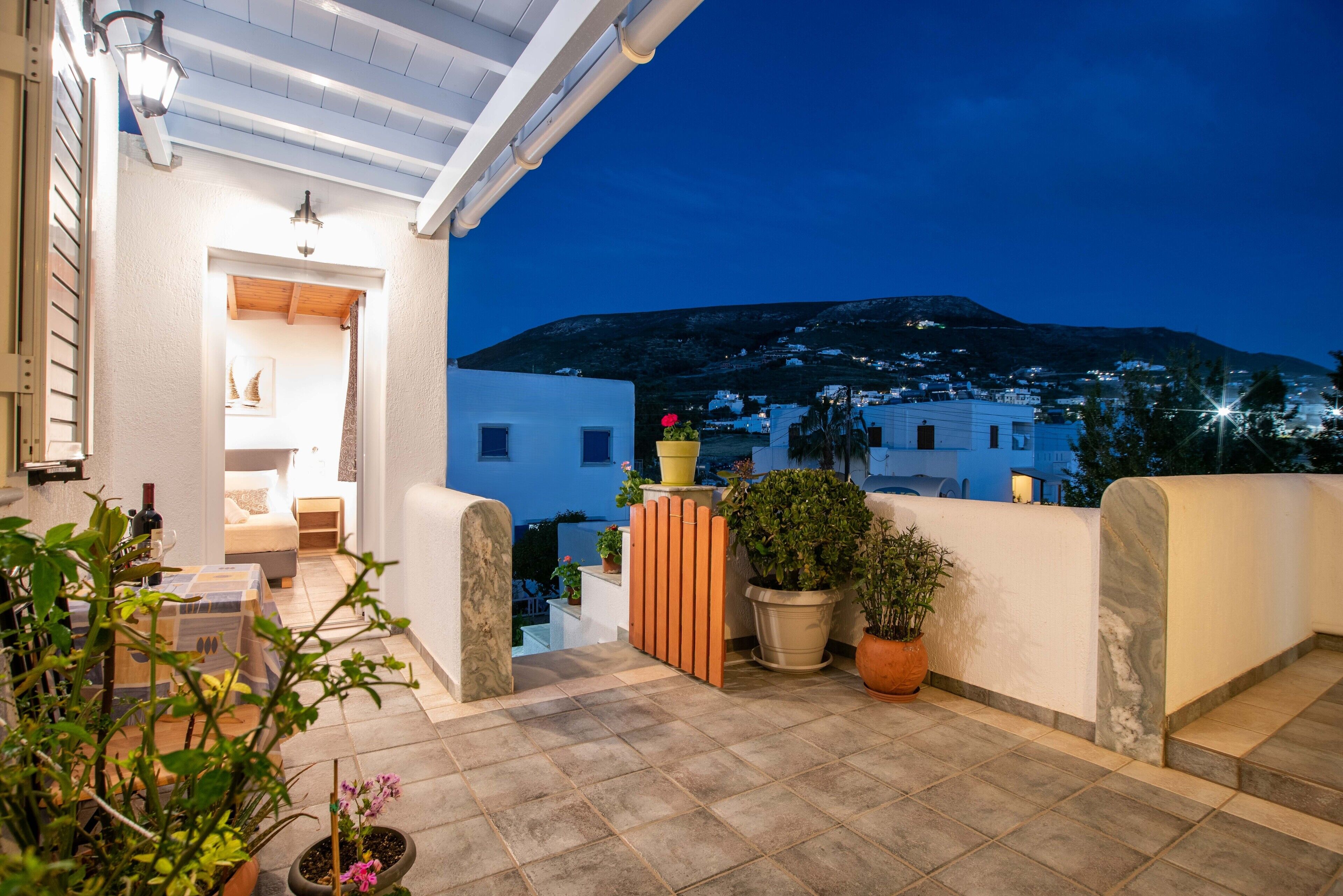 Una terraza con plantas en macetas, un portón de madera y vistas a una colina al anochecer.