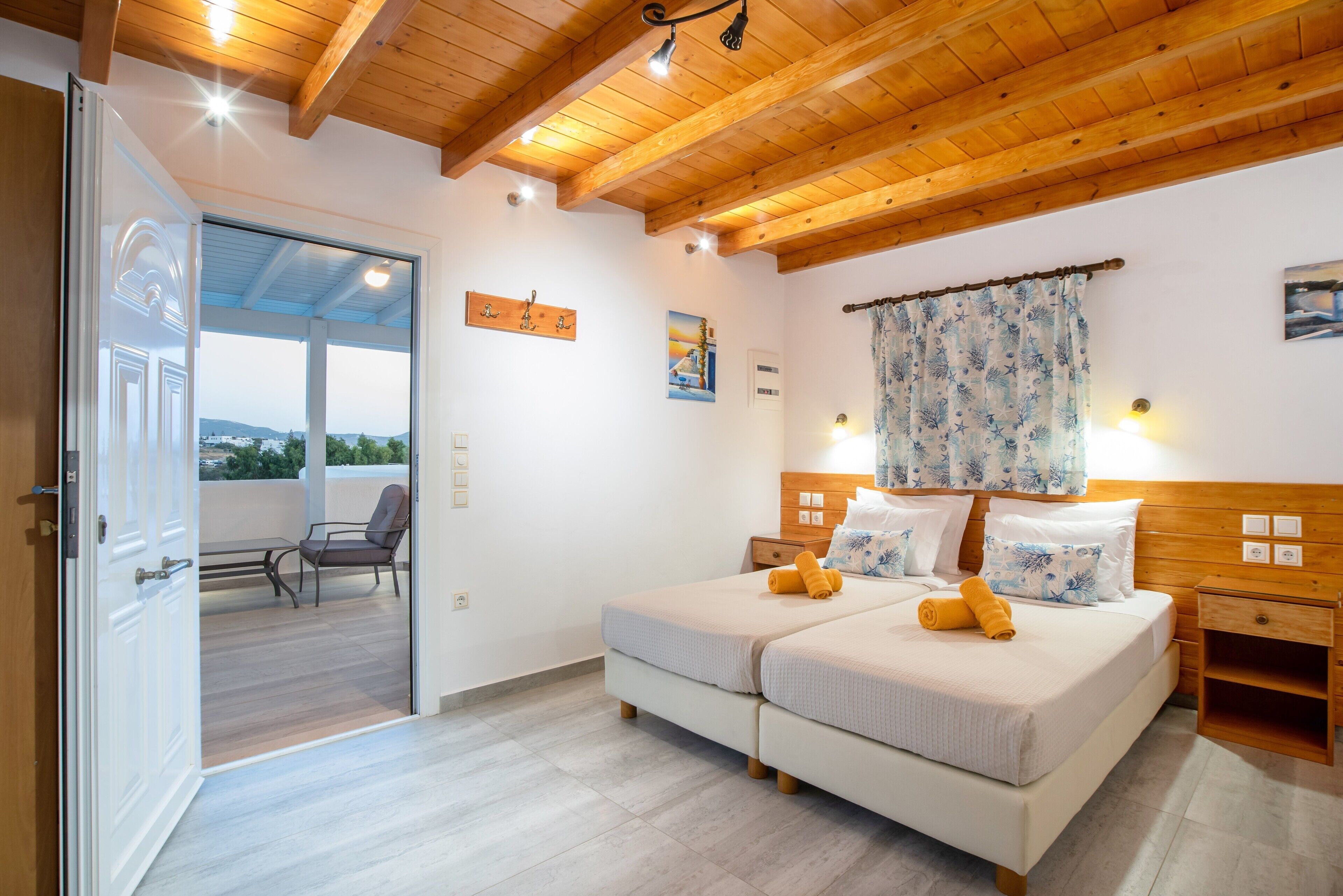 Een slaapkamer met twee bedden, houten balken in het plafond, een balkon met een stoel en uitzicht op het landschap.