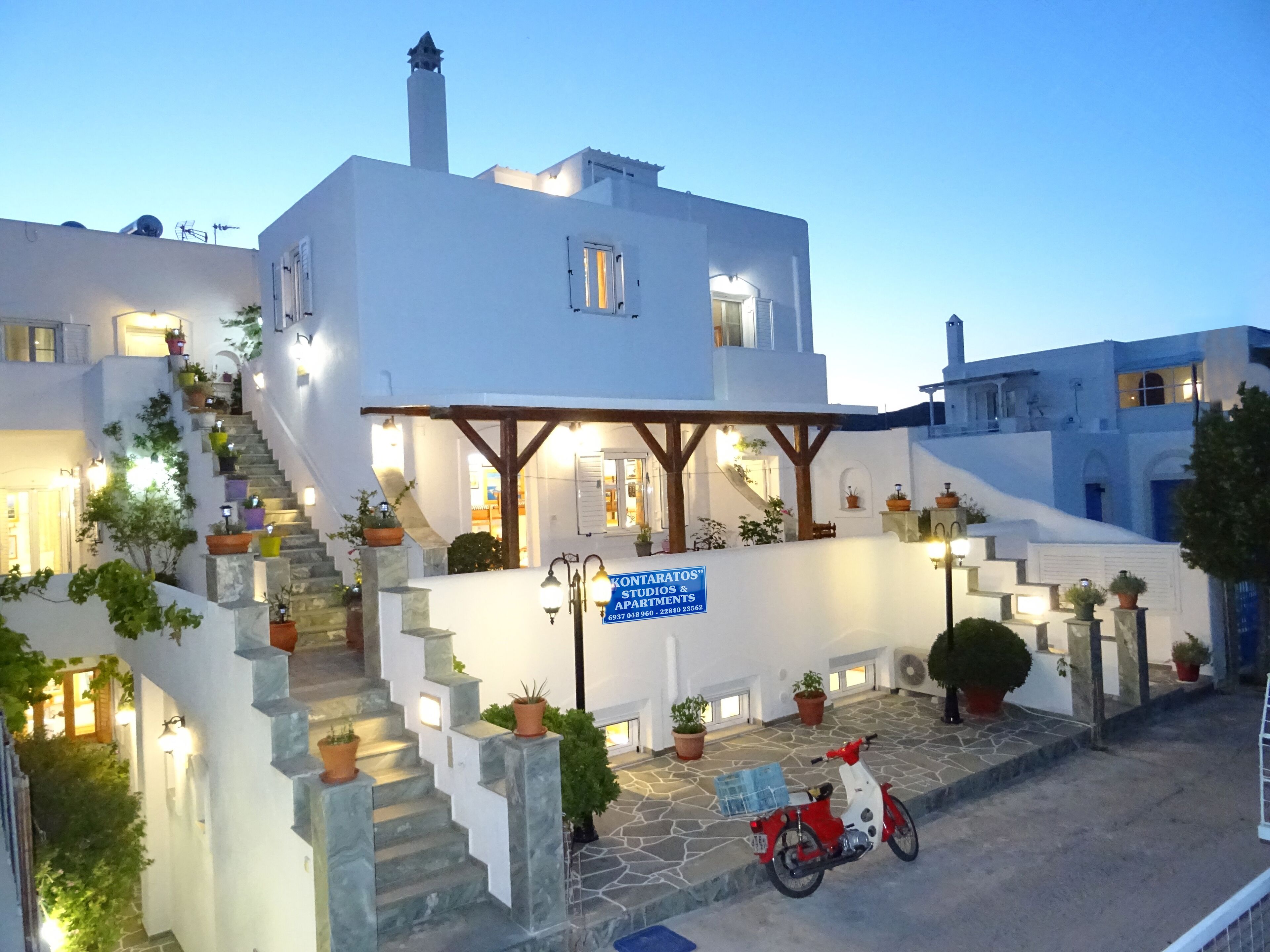 A white building with a sign for "Konstantatos Studios & Apartments" and a red scooter parked in front.