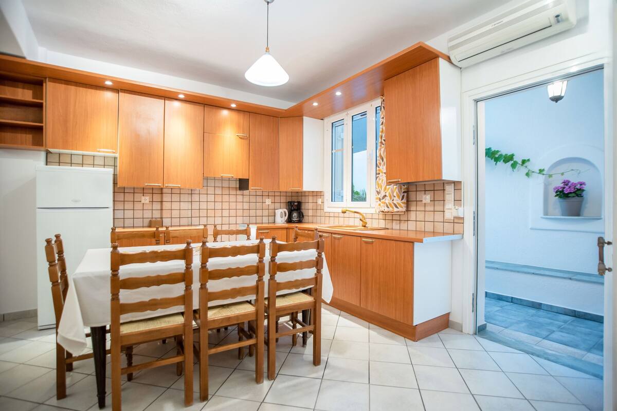 A modern kitchen with wooden cabinets, a tiled backsplash, a dining table with chairs, and a window with a view.