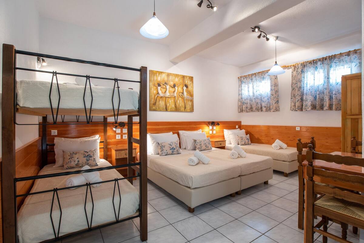 A hotel room with a bunk bed, a double bed, and a sofa bed. There are two bedside tables with lamps, a painting on the wall, and a window with curtains.