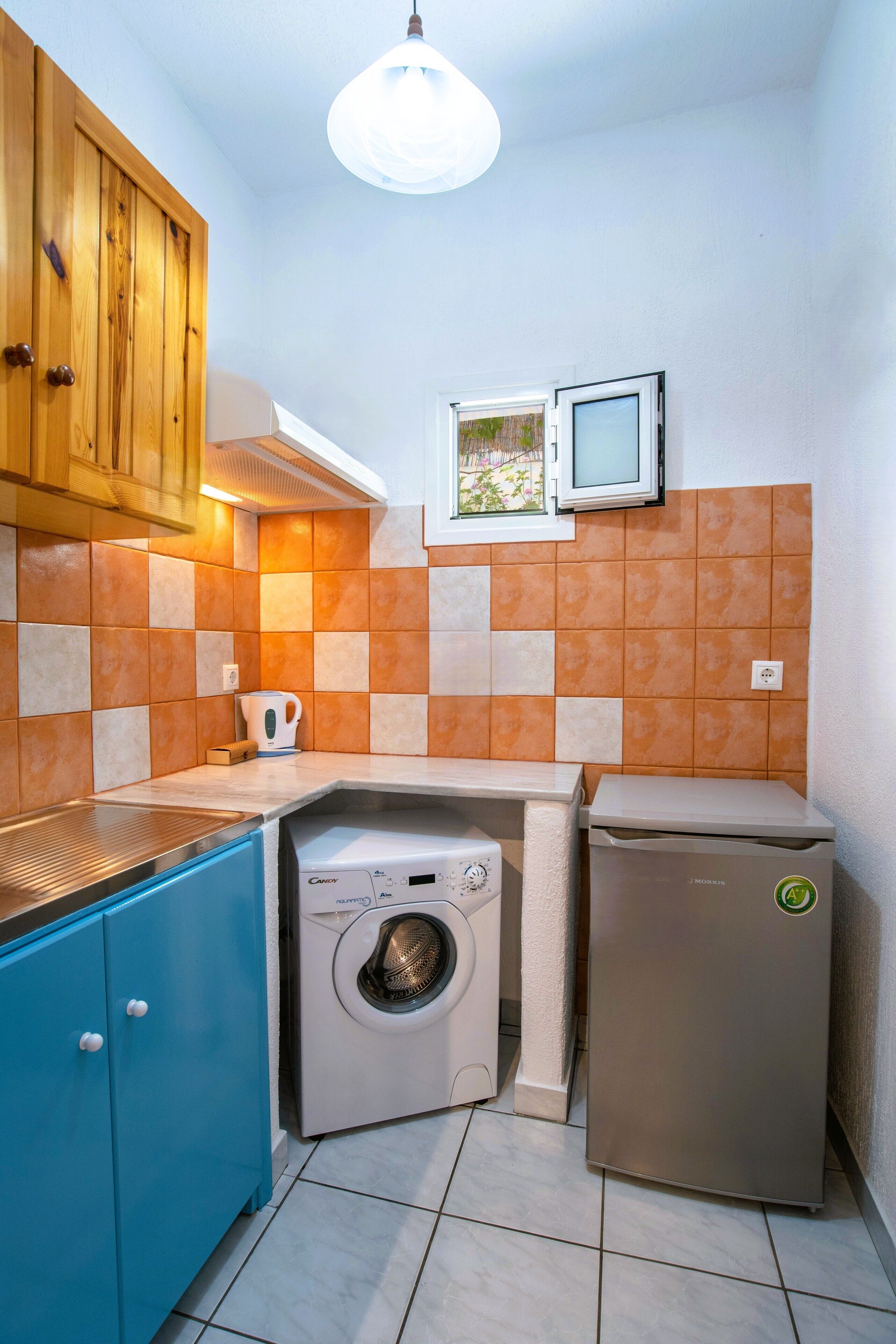 A compact kitchen with a washing machine, a small refrigerator, and a microwave.