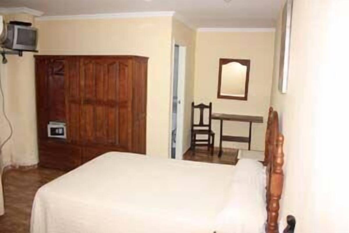 A bedroom with a bed, wooden wardrobe, a desk, and a chair.