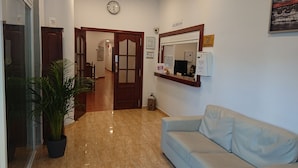 A reception area with a reception desk, a clock, a reception sign, a potted plant, and a light-colored sofa. - Hotel Manantiales (Torremolinos)