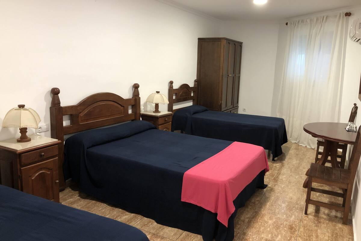 A hotel room with two beds, a nightstand, a cabinet, a table, and a chair.