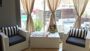 A corner seating area with two cushioned chairs, a small table with magazines, and a view of the street outside. - Hotel Manantiales (Torremolinos)