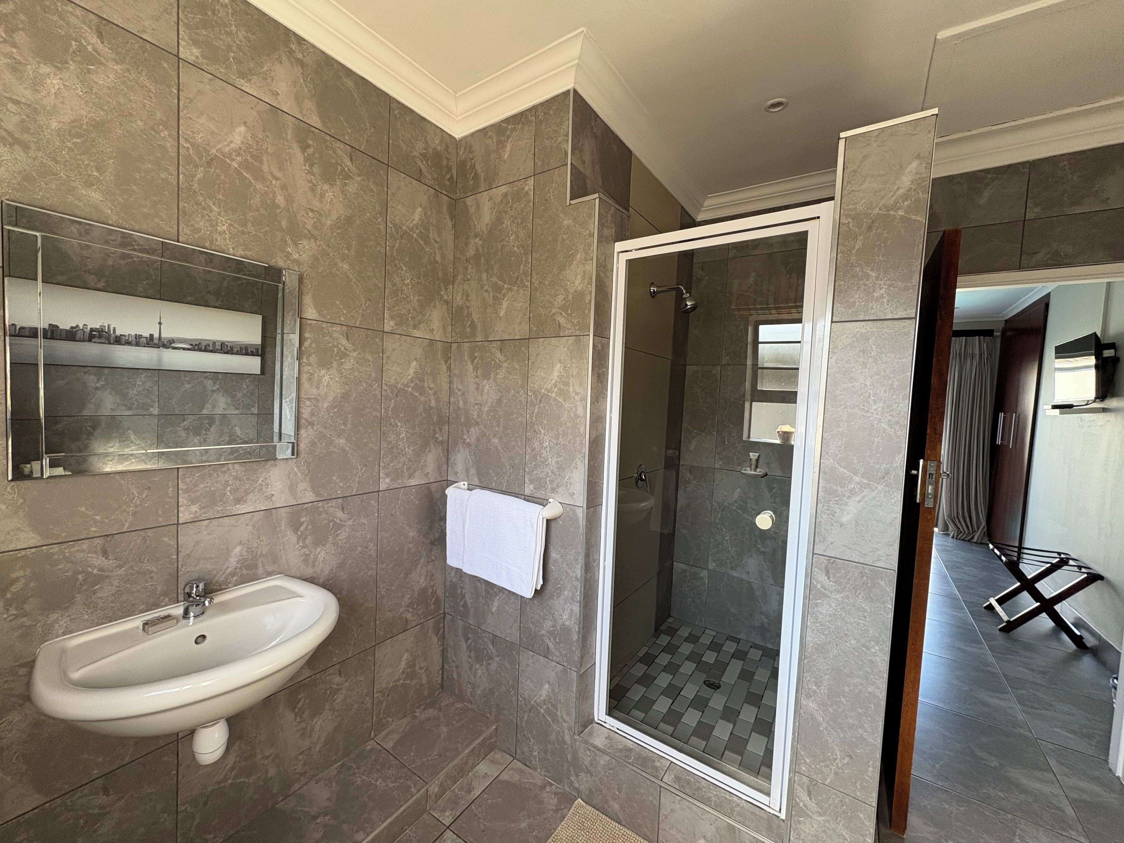 A modern bathroom with a sink, a glass shower enclosure, and a mirror with a cityscape picture.