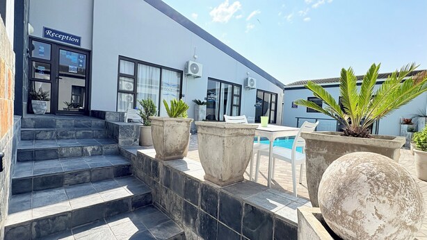 A reception area with a staircase leading to a poolside area, potted plants, and a clear blue sky. - Le Blue Guesthouse (Gqeberha (Port Elizabeth))