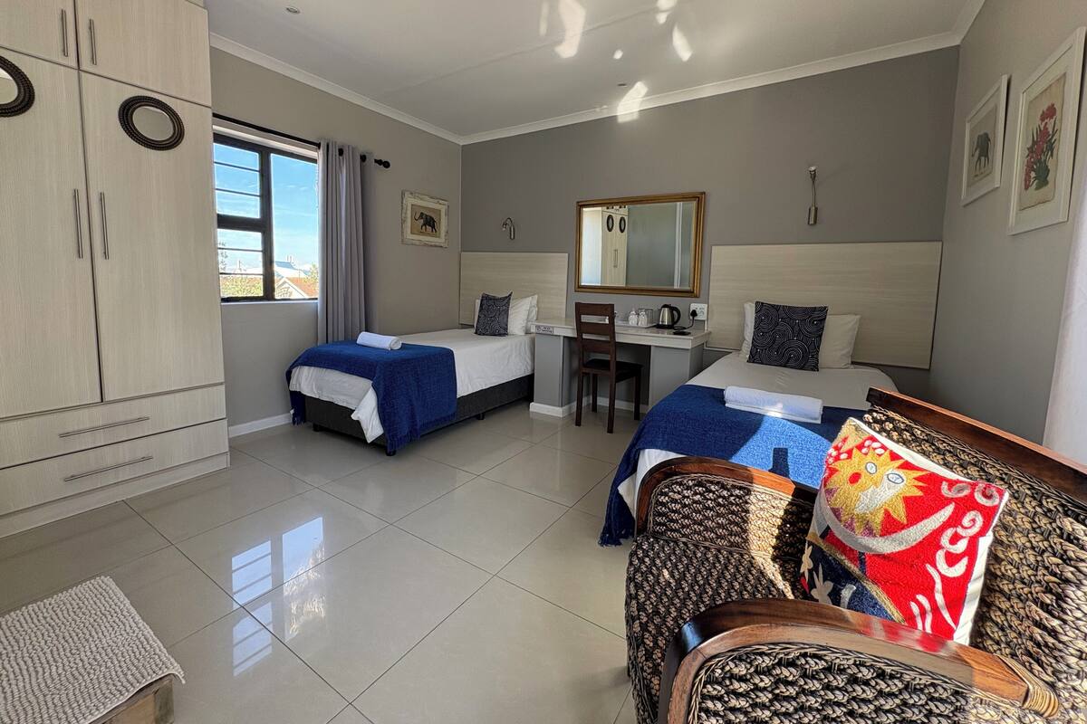 A hotel room with two beds, a desk, a wardrobe, and a large window.