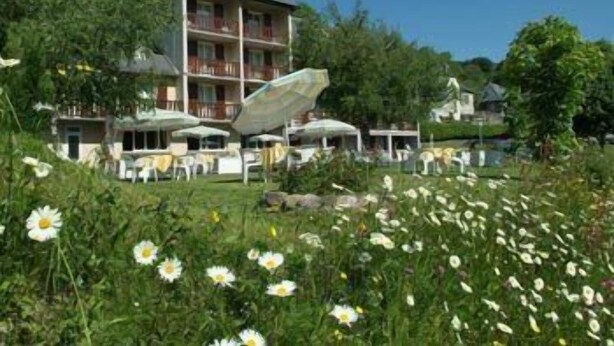 Un hotel de varios pisos con terraza al aire libre y jardín lleno de flores.