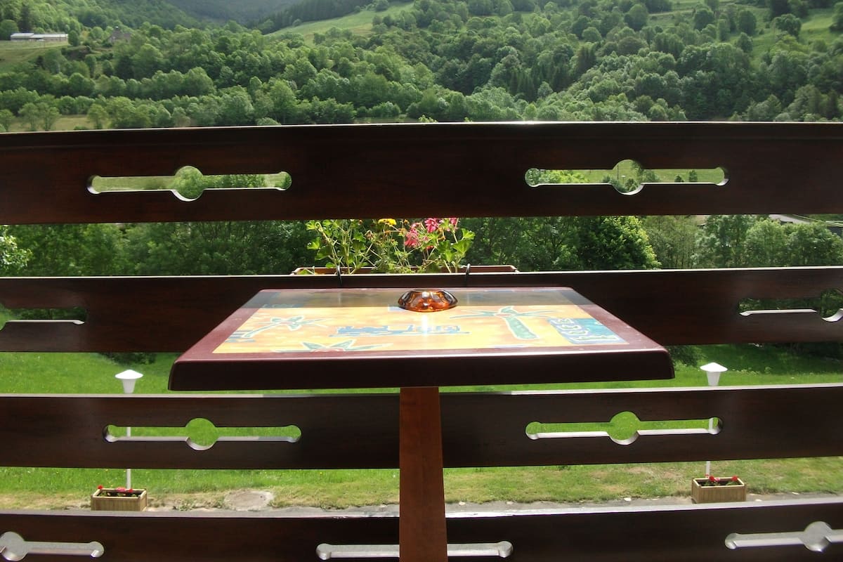 Eine hölzerne Bank mit Tisch davor, mit Blick auf ein üppiges, grünes Tal und sanfte Hügel im Hintergrund.