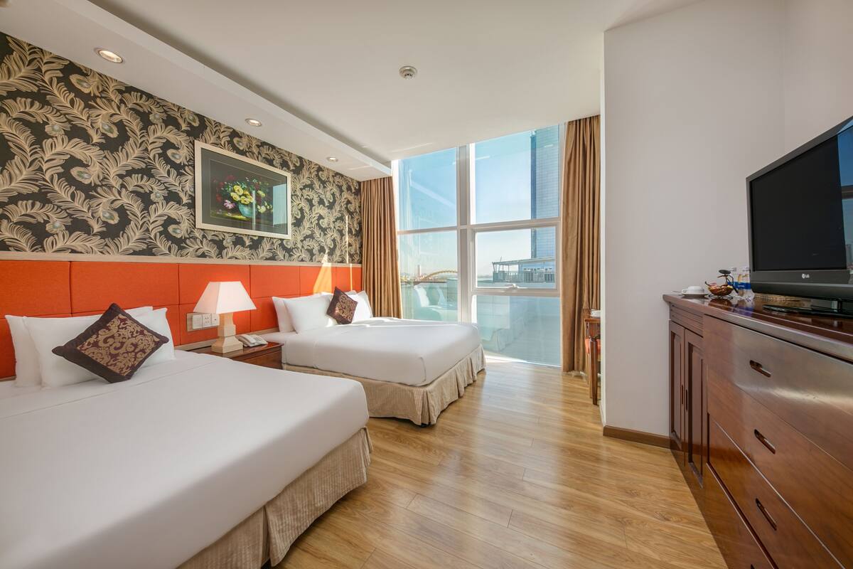 A hotel room with two beds, a large window with a city view, a TV, and a wooden cabinet.