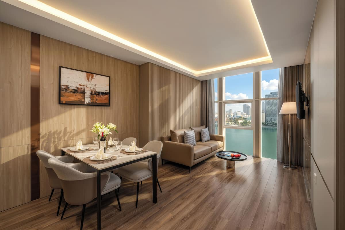 A modern living room with a dining area, wooden flooring, a sofa set, a flat-screen TV, and a large window offering a city view.