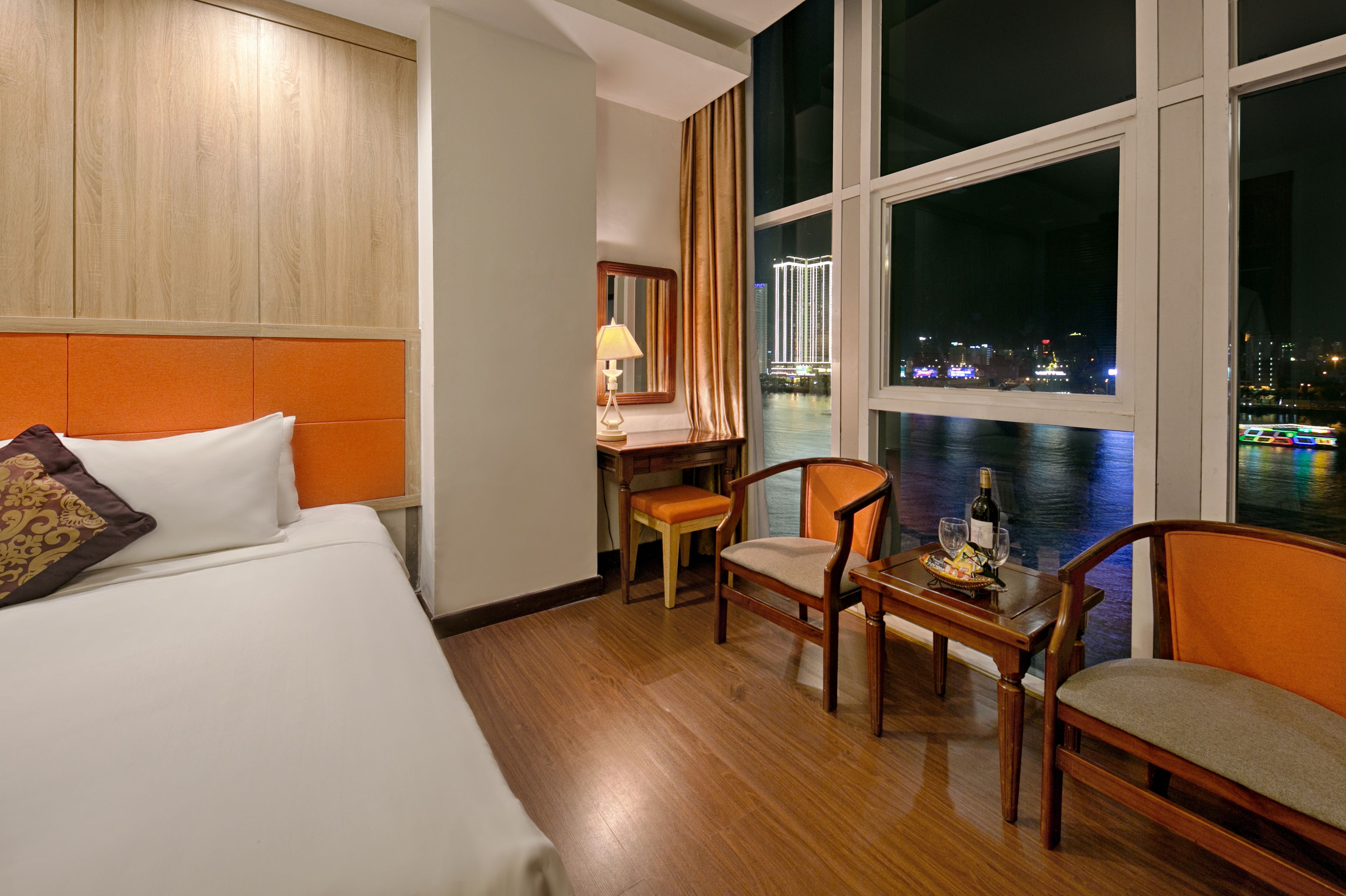A hotel room with a bed, a desk, a chair, and a view of a cityscape at night.