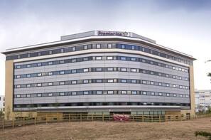 A modern hotel with a curved facade, multiple floors, and a prominent signage. - Premier Inn Manchester Airport - M56/J6 Runger Lane North (Manchester)