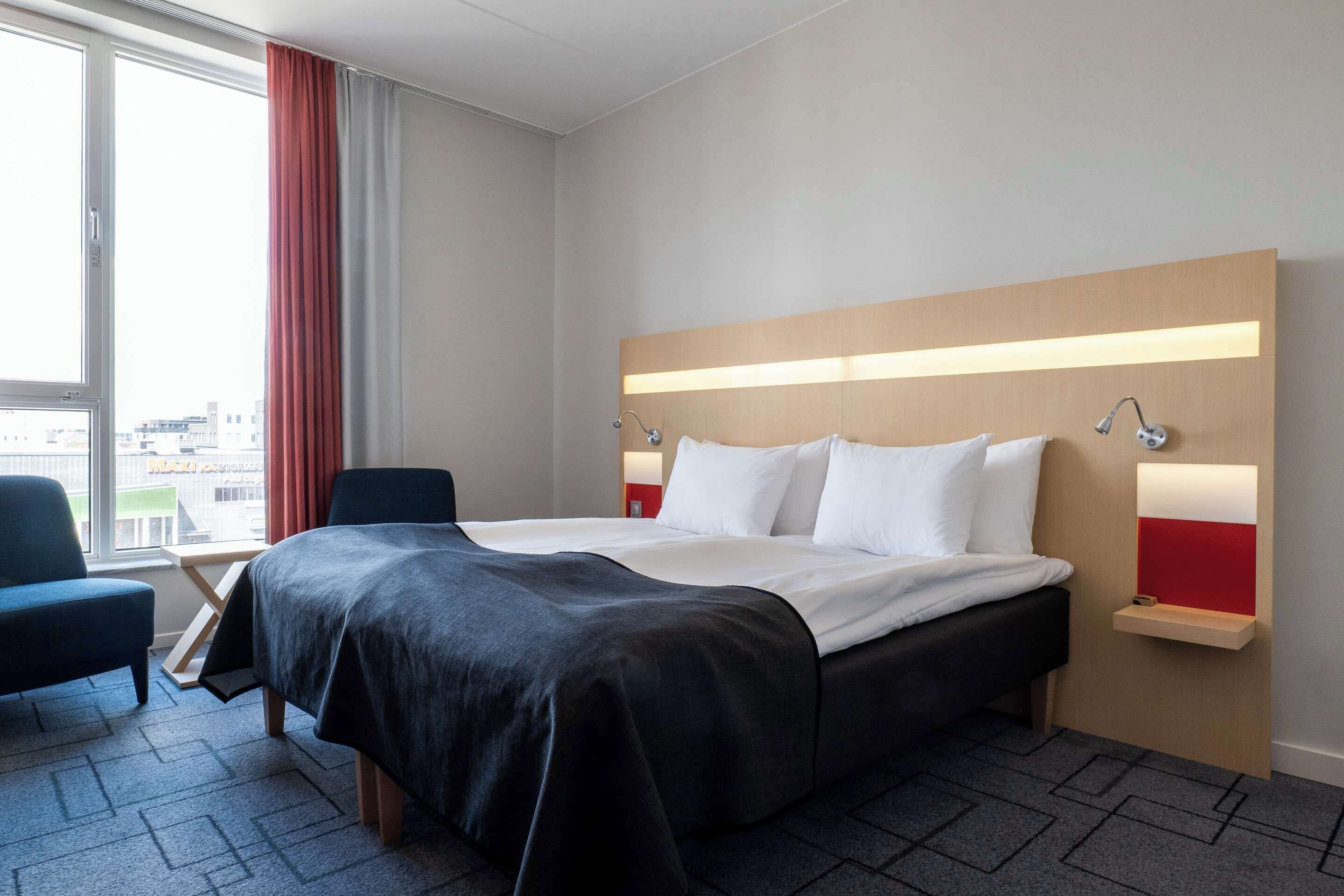 A modern hotel room with a large bed, a desk, and a chair.