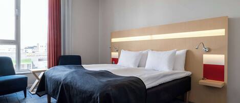 A modern hotel room with a large bed, a desk, and a chair.